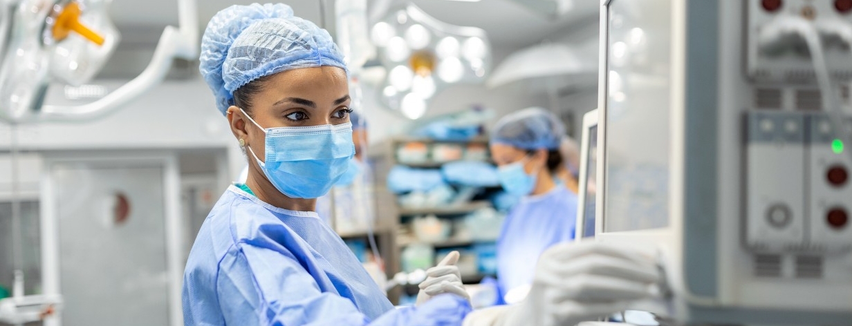 Anesthetist Working In Operating Theatre Wearing Protecive Gear checking monitors while sedating patient before surgical procedure in hospital